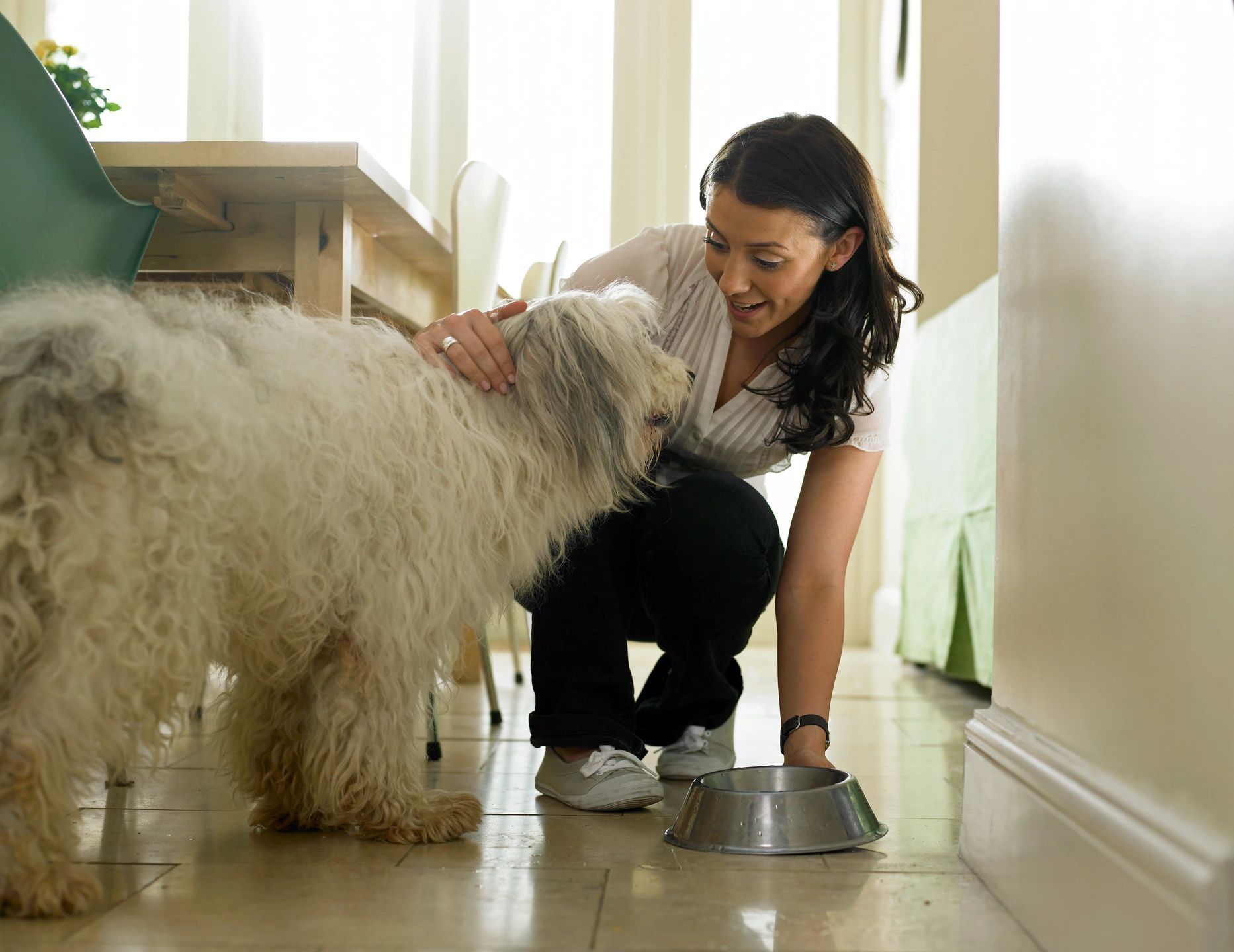 A woman petting her dog while standing on the floor.